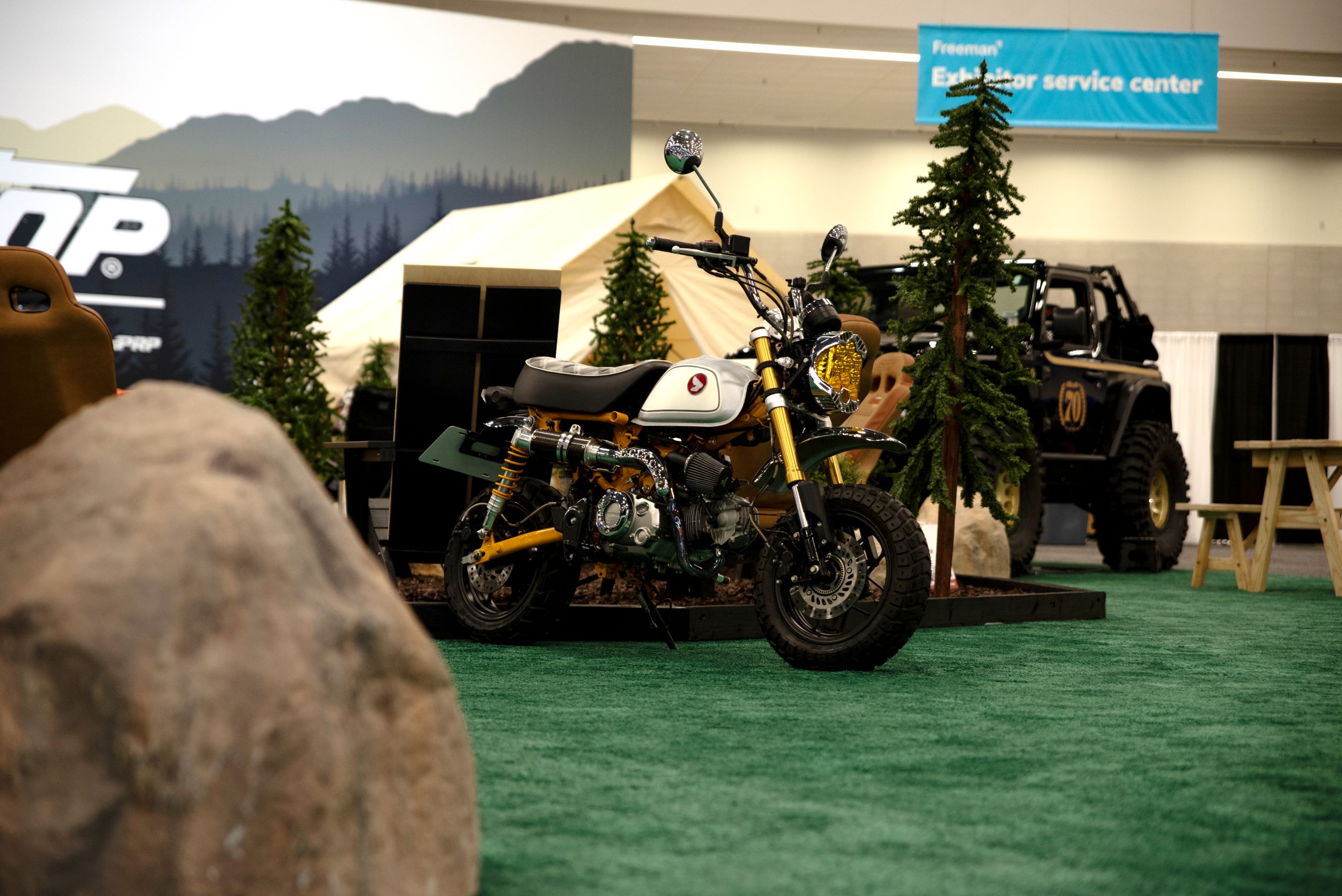 A customized Honda Monkey mini-bike with a white tank and yellow frame displayed on green turf at the SEMA show.